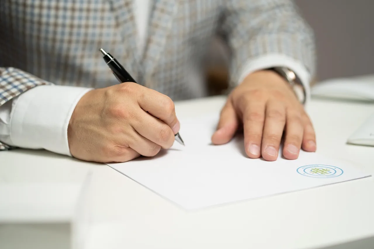 Personne en train de rédiger et signer des formalités administratives sur un bureau.