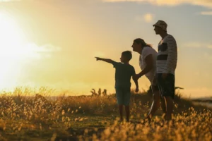 Famille en contre-jour dans une prairie au coucher du soleil avec un enfant pointant du doigt