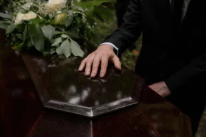 Main posée sur un cercueil en bois verni orné de fleurs lors d'une cérémonie de funérailles